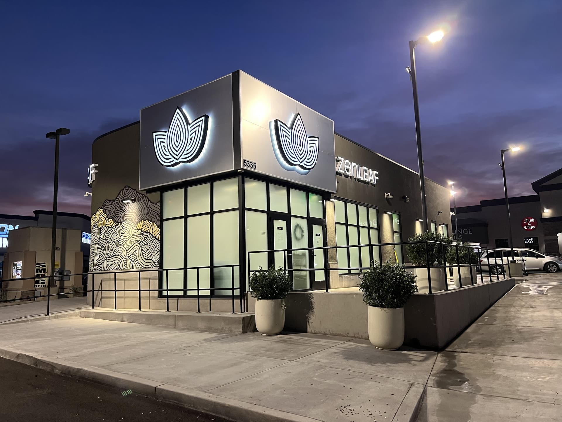 Modern storefront of a business at dusk with illuminated lotus logos and large windows. The sky is deep blue, creating a calm and inviting atmosphere.